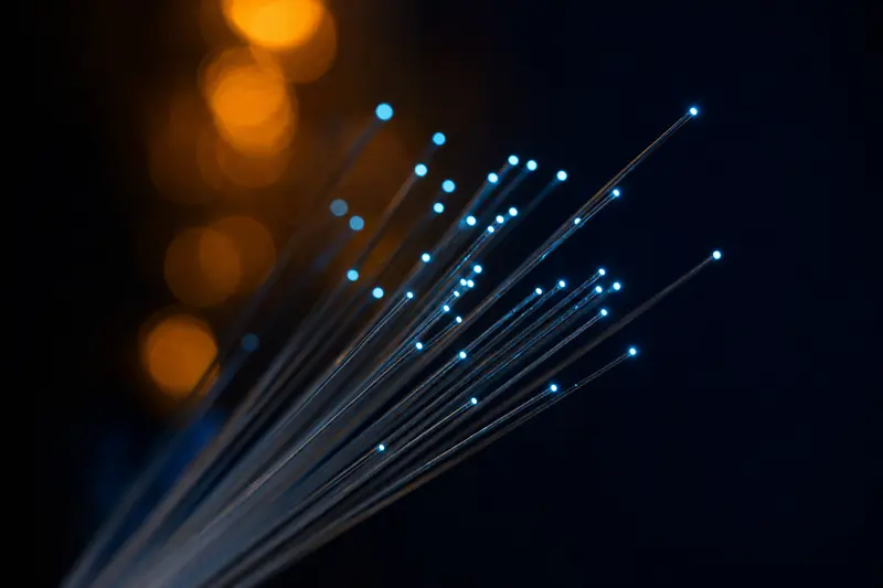 A macro view of a fanned bundle of optical fibre strands, each tipped with a bright point of light against a near-black background.